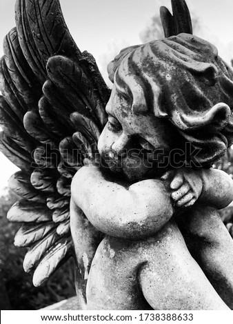 Close up of a little weathered angel statue on a grave stone. Black and white photo. Black and white cherub photo