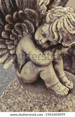 Close up of a little weathered angel statue on a grave stone. Sitting Cherub, weathered and worn sculpture on a grave. 