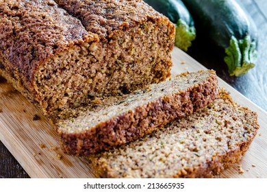 Close up of loaf of homemade zucchini bread sitting on wooden cutting board with fresh zucchini squash