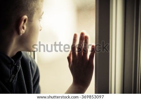 Close up Lonely Orphan Boy in an Orphanage Looking Outside While Holding the Glass Window.