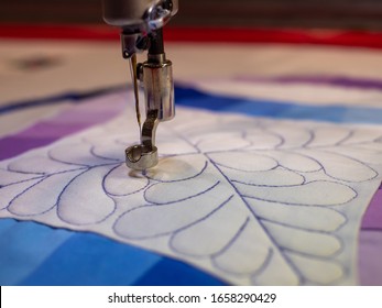 Close up of a long arm quilting machine top stitching a feathered design into a double wedding ring quilt in blue and purple