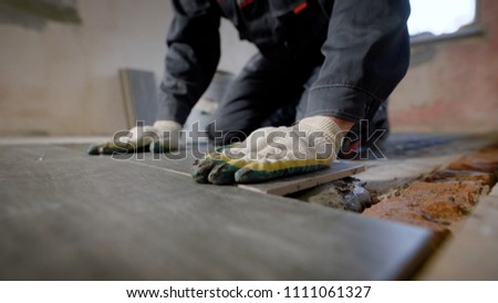 Close look at the constuction worker laying down the tile on cemented floor. Measuring the evenness of the floor with a waterpas.