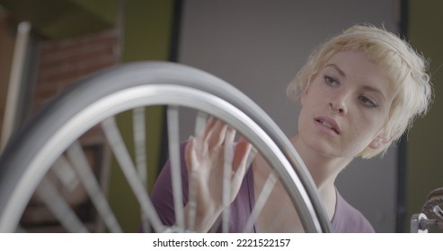 Close Up Looking Across Bicycle Wheel As Young Blonde Woman Checks The Tire In An Urban Loft