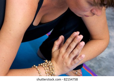 Close up looking down at woman in yoga garland pose with hands in namaste position.