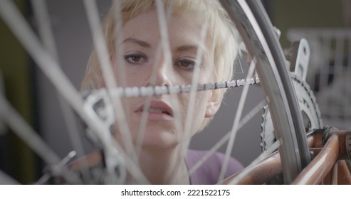 Close Up Looking Through Moving Spokes At Young Woman Working On Bike Wheel And Chain In An Urban Loft