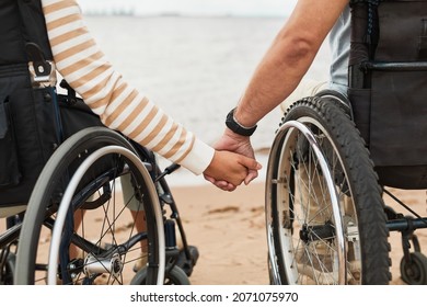 Close up of loving couple in wheelchairs holding hands on beach by ocean, copy space