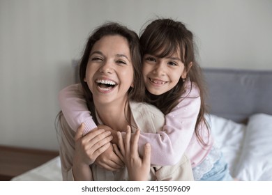 Close up of loving hispanic mother spend time at home, sit on bed in bedroom with cute daughter, enjoy tender moment, cheerful cute girl embrace happy mom looking at camera, express love and warmth - Powered by Shutterstock