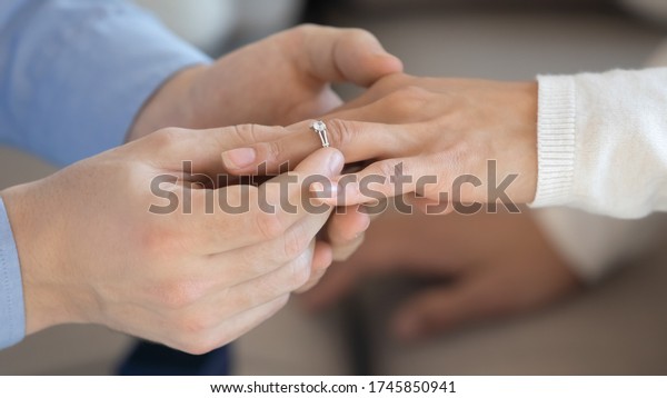 Close up of loving man put beautiful diamond\
wedding ring propose to beloved woman finger, affectionate male\
make marriage proposal to girlfriend or female lover, engagement,\
marry me concept