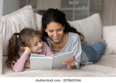 Close Up Loving Mother With Cute Daughter Reading Book Aloud Together, Enjoying Interesting Fairy Tale Story, Relaxing Lying On Couch At Home, Smiling Mom With Kid Engaged In Educational Activity