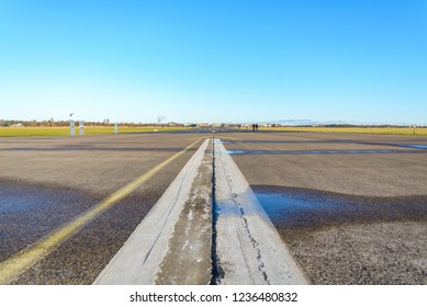 Close Up Low Angle Diminish Perspective View Of Cracking Asphalt Road, Airport Runway Or Airfield At Tempelhof Field Park, Former Airport, With Clear Blue Sunny Sky In Berlin, Germany.