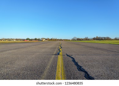 Close Up Low Angle Diminish Perspective View Of Cracking Asphalt Road, Airport Runway Or Airfield At Tempelhof Field Park, Former Airport, With Clear Blue Sunny Sky In Berlin, Germany.