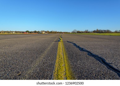 Close Up Low Angle Diminish Perspective View Of Cracking Asphalt Road, Airport Runway Or Airfield At Tempelhof Field Park, Former Airport, With Clear Blue Sunny Sky In Berlin, Germany.