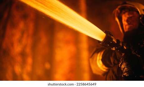 Close Up Low Angle Portrait of a Brave Professional Firefighter Using a Firehose to Fight a Raging Dangerous Forest Fire. Fireman Using High-Pressure Water Hose With Hands and Battling Bushfire. - Shutterstock ID 2258645649