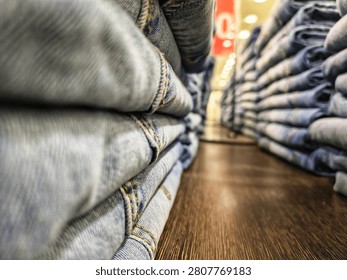 Close up low angle view between two large stacks of neatly folded blue denim jeans on a wooden display shelf in a retail clothing store.