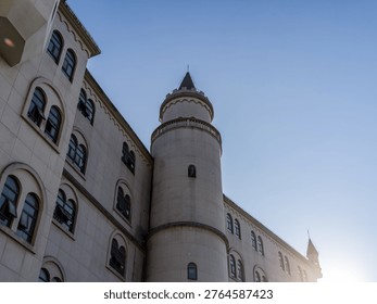Close low angle view of a classic white castle-style building featuring a prominent round turret, arched windows, and dark roofing under a clear sky. The scene represents historic aesthetics, prestigious academic environments, European architecture, and romantic building design.