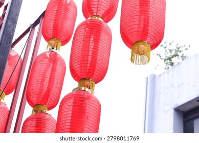 Close up low angle view of large cylindrical red Chinese lanterns with gold tassels hanging from red metal pole against white sky
