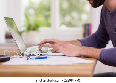 Close Up Low Angle View Of A Man Working From Home On A Laptop Computer Sitting At A Desk Surfing The Internet