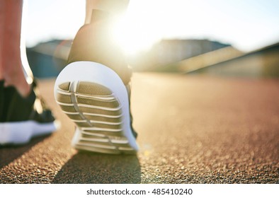 Close Up Low Angle View Of Running Shoes With While Soles On An Empty Road As The Sun Highlights The Distance