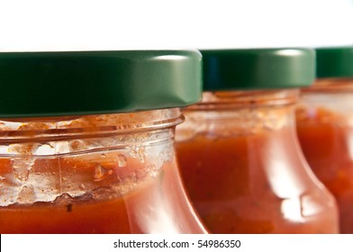 Close And Low Level Angle Capturing The Top Portions Of A Line Of Clear Jars Containing Pasta Sauce. First Jar In Focus.