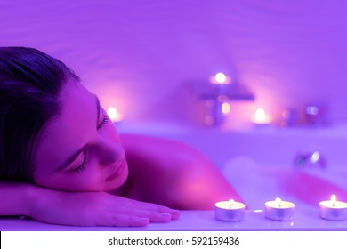 Close Up Low Light Portrait Of Young Woman Relaxing In Foam Bath.Low Colorful Candlelight Ambient With Candles On Bath Tub.