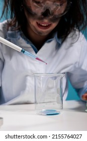 Close up of lunatic silly looking maniac biochemist using dropper to experiment with toxic chemical compounds. Crazy lab worker dripping blood drops in glass beaker while conducting dangerous test.