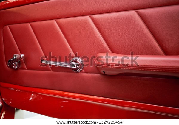 Close up\
of luxury car door panel. Interior of prestige classic sports car.\
Red perforarated leather cockpit. Car door interior armrest with\
window control lever and door lock\
handle.