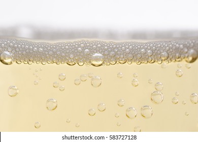 Close up (macro) of  champagne glass, filled with sparkling white wine.  Rising bubbles topped by layer of froth. Eye level shot.