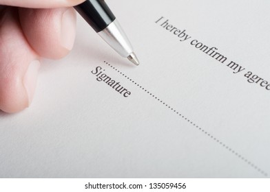 Close Up (macro) Shot Showing Fingers Of A Male Hand, Holding A Pen, Poised To Sign On The Dotted Line Of A Legal Document Or Contract.