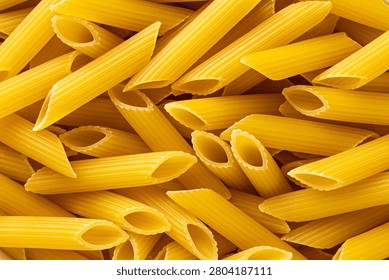 Close macro texture of uncooked penne pasta tubes filling the frame as golden dry food background