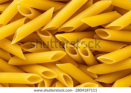 Close macro texture of uncooked penne pasta tubes filling the frame as golden dry food background