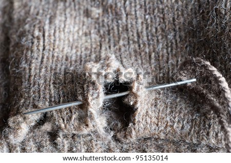 Close up (macro) of a threaded needle, darning a hole in an old frayed woolen garment.  To suggest needlework, recycling or frugality during recession.