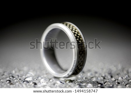 Close up macro view of a carbon fiber and tungsten carbide wedding ring with a black and gray background.