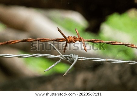 Close up macro view of sharp barbed wire fence showing stark contrast between rusty old metal strand and shiny new silver strand conveying harsh forbidding sense of strict boundary
