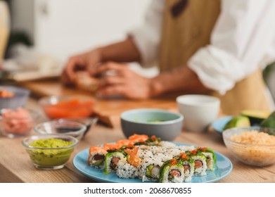 Close up making sushi rolls process. Rolls on a plate, Ingredients for sushi on a table, and master's hands on background. Sushi delivery