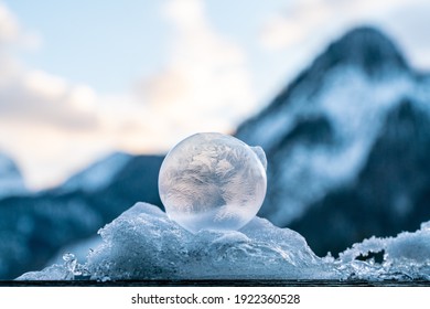 close up makro shot of beautiful frozen bubbles bedded on a pile of white snow and blue ice with a delicate structure of ice flowers back-lit by the rising sun with mountains in the background