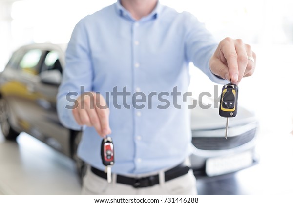 Close up of male adult car dealer\
holding car keys in each hand, offers a choice of two\
keys