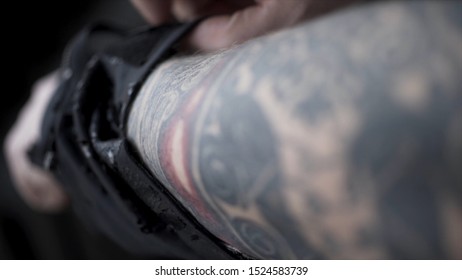 Close Up Of The Male Arm With Black Tattoo And A Man Putting On Black Old Arm Warmer, Art Concept. Action. Man With A Large Tattoo On His Arm Pulling Up Black Fabric Arm Warmer.