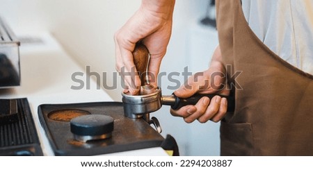 Close up of male barista making coffee while holding tamper in the hand, going to press ground coffee in holder. Coffee preparation service concept
