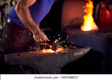 Close Up Of Male Blacksmith Hammering Metalwork On Anvil With Sparks And Blazing Forge In Background - Powered by Shutterstock