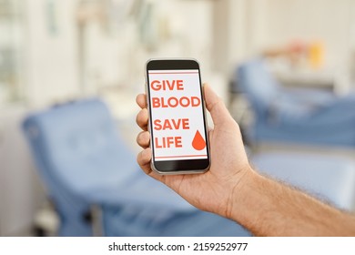 Close Up Of Male Blood Donor Holding Smartphone With Give Blood Save Life Slogan At Donation Center, Copy Space