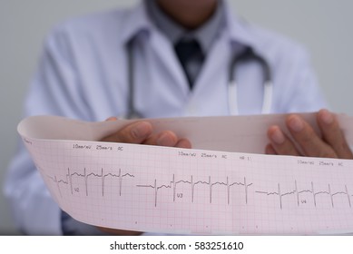 Close Up Of Male Cardiologist Doctor Or Medical Student In White Coat With Stethoscope Holding And Reading Ekg Paper Print Report Of Heart Disease Patient