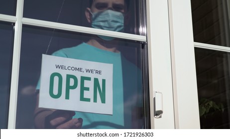 Close up of the male Caucasian hands turning a signboard on the glass door of the shop from CLOSED to OPEN. Reopening of a small business activity after quarantine covid-19 emergency.