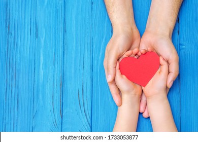 Schließen Sie männliche und kinderreiche Hände, die das rote Herz über dem hölzernen blauen Hintergrund halten. Konzept der Familie und Vatertag.