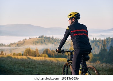 Close Up Male Cyclist In Cycling Suit Riding Bike With Hills On Background. Man Bicyclist Wearing Safety Helmet And Glasses While Enjoying Bicycle Ride In Mountains In The Morning. Back View