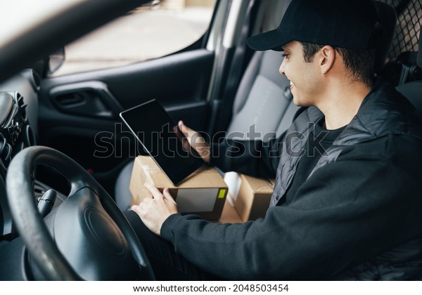 Close up of a\
male delivery person sitting on a driver\'s seat checking delivery\
information on a digital\
tablet