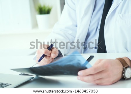 Close up of male doctor looking at x-ray or roentgen image and making notes in medical form.
