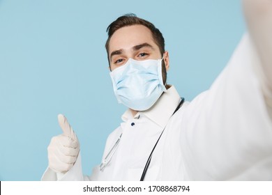 Close up of male doctor man in medical gown face mask gloves isolated on blue background. Epidemic pandemic coronavirus 2019-ncov sars covid-19 flu virus Doing selfie on mobile phone showing thumb up - Shutterstock ID 1708868794