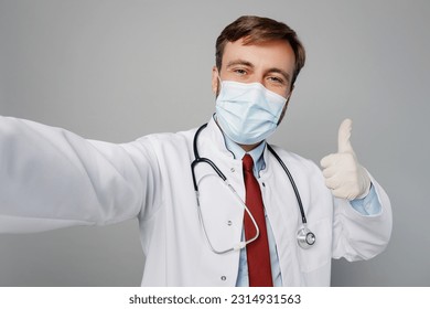 Close up male doctor man wears white medical gown suit mask work in hospital do selfie shot pov on mobile cell phone show thumb up isolated on plain grey background studio. Healthcare medicine concept - Shutterstock ID 2314931563