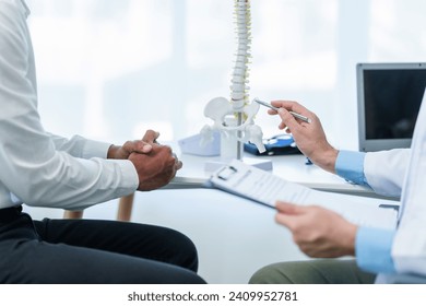 Close up male doctor and patient people in a medical office, spine model, possibly discussing spinal condition or syndrome with the patient. - Powered by Shutterstock