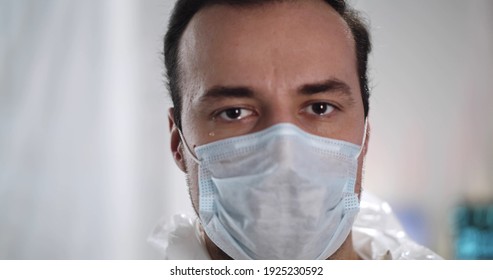 Close Up Of Male Doctor In Protective Mask Crying And Looking At Camera. Portrait Of Man Medical Worker Wearing Safety Mask Standing In Hospital With Tears On His Face